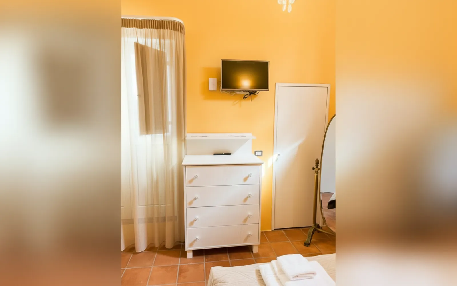 La TV e la cassettiera bianca fra le pareti color albicocca